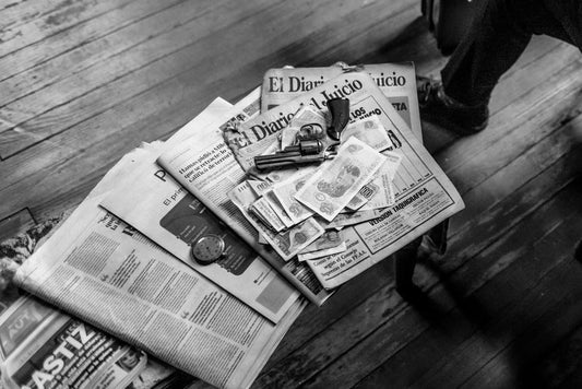 Black and white image featuring currency, newspapers, and a revolver on a wooden surface.